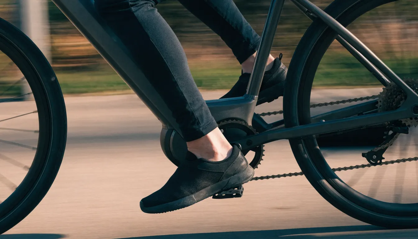 Bisiklet yolunda elektrikli şehir bisikletinin pedalını çeviren bacakların yandan yakın çekimi, kadroda motor ve batarya görünüyor